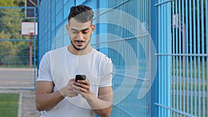 Middle eastern indian man holding phone in hands texting message or using mobile apps, checking social media