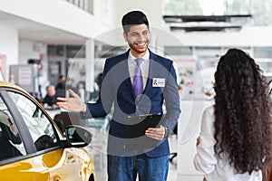 Middle-eastern lady choosing new car, having conversation with sales manager
