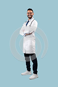 Middle-Eastern Male Doctor Posing Wearing White Uniform Over Blue Background