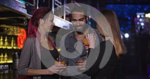 Middle Eastern man coming to two young Caucasian women drinking cocktails in night club. Confident handsome guy flirting
