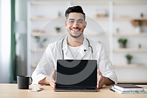 Middle-eastern man doctor showing laptop with blank screen, mockup