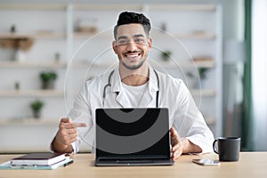 Middle-eastern man doctor showing laptop with blank screen, mockup