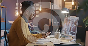 Middle Eastern man making online video call talking to woman in hijab using computer and earphones in office at night