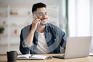 Middle-eastern man working online, using laptop and mobile phone