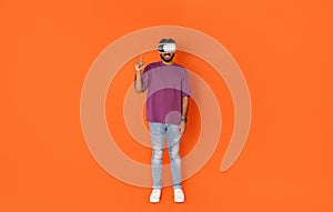 Middle eastern millennial guy using VR goggles on orange