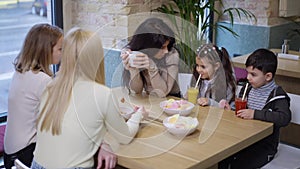 Middle Eastern young mother little daughter and son sitting in cafe with Caucasian women talking eating drinking