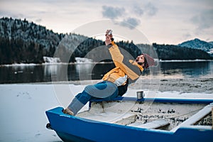 In the middle of nature with a big lake and snowy mountain and forest young man with orange jacket taking pictures of