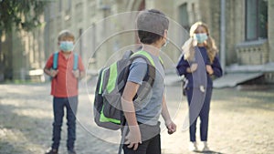 Middle school students in face masks having fun on schoolyard on sunny day. Portrait of relaxed positive Caucasian