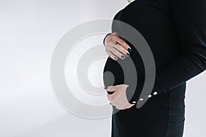 Middle selection on pregnant woman puts hands on her belly. Female in black bodycon dress. White background