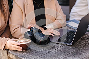 Middle selection of two women drinks coffee in cafe and checking pictures at the laptop. Mirrorless camera on table