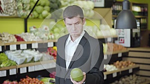 Middle shot of concentrated Caucasian man choosing pomelo in grocery. Portrait of young confident guy buying healthful