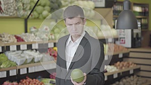 Middle shot of concentrated Caucasian man choosing pomelo in grocery. Portrait of young confident guy buying healthful