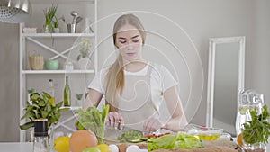 Middle shot of concentrated female chef cutting ingredients for healthful salad on board. Portrait of serious young