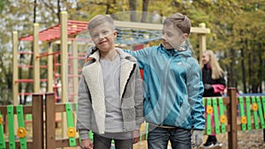 Middle shot of joyful Caucasian brothers hugging and looking at camera smiling standing in autumn park outdoors. Happy