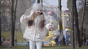 Middle shot of joyful little girl dancing in autumn park. Portrait of cheerful pretty child jumping and gesturing on