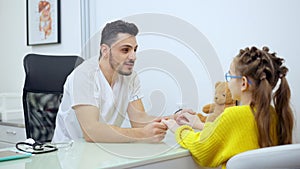 Middle shot of joyful male pediatrician holding hands of patient talking and smiling. Positive handsome Middle Eastern