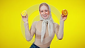 Middle shot of joyful pretty redhead woman closing eyes with half oranges smiling and looking at camera. Portrait of