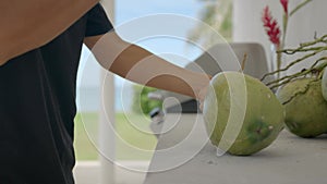 Middle shot of a man cutting a coconut with big knife, on the table near outdoorsman grill, outdoors on the open kitchen