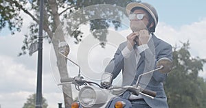 Middle shot portrait of positive confident man putting on helmet in slowmo as sitting on motorcycle outdoors. Smiling
