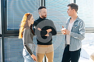 Middle shot portrait of three serious young business people having fun conversation during coffee break in modern office