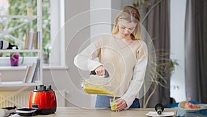 Middle shot of slim gorgeous young woman pouring fruit smoothie in glass and drinking healthful vitamin drink. Portrait