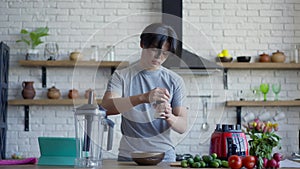 Middle shot of young Asian man salting healthful spring salad in kitchen in the morning. Portrait of confident handsome