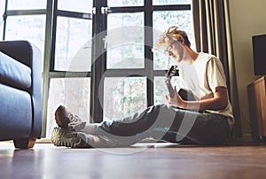 Middle shot of young man plays on guitar sitting on the floor in