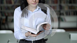 Middle shot young woman flipping a encyclopedia on background of library shelves