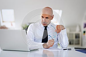 Mide aged businessman sitting at office desk and using laptop for work photo