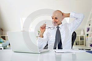 Mide aged businessman sitting at office desk and using laptop for work photo