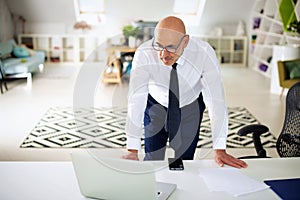 Mide aged businessman standing at office desk and using laptop and having video call photo