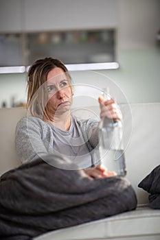 Midlle aged woman at home with a bottle of strong alcohol photo