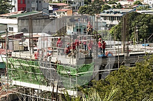 A midrise office building under construction, with construction workers in red