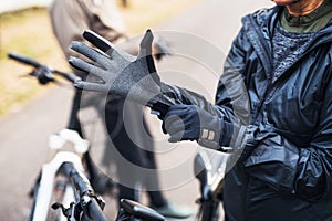 A midsection of active senior couple standing outdoors with electobikes, putting on gloves.