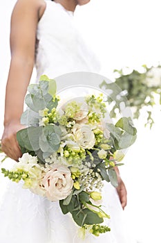 Midsection of african american bride holding bouquet standing in sunny garden