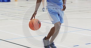 Midsection of african american male basketball player bouncing ball at indoor court, slow motion