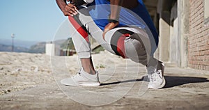 Midsection of african american man tying shoelaces during exercise outdoors on beach