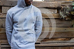 Midsection of african american man wearing grey hooded sweatshirt against wooden fence, copy space