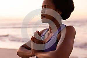 Midsection of african american mature woman with eyes closed meditating in prayer pose against sea