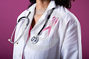 Midsection of african american mid adult doctor with breast cancer awareness ribbon and stethoscope