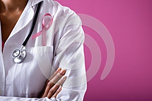 Midsection of african american mid adult doctor with pink breast cancer awareness ribbon, copy space