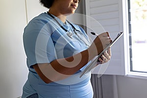 Midsection of african american mid adult female nurse writing on clipboard in hospital