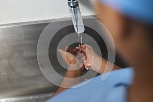 Midsection of biracial female doctor wearing scrubs washing hands in operating theatre
