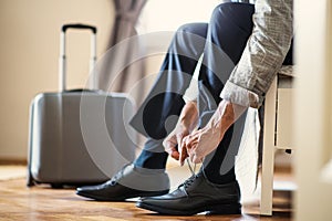 Midsection of businessman on a business trip sitting in a hotel room, tying shoelaces.