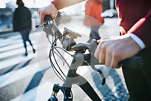 A midsection of businessman commuter with electric bicycle traveling to work in city.