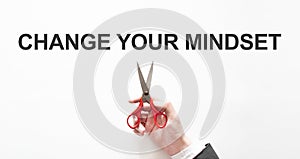 Midsection of businessman cutting the word Change Your Mindset on paper with scissors over gray background