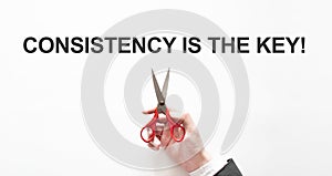 Midsection of businessman cutting the word Consistency is the key on paper with scissors over gray background