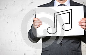 Midsection of businessman holding placard with music note sign while standing against white brick wall