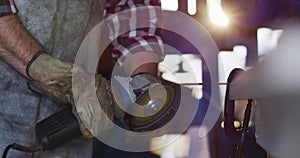 Midsection of caucasian male knife maker in workshop using angle grinder