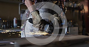 Midsection of caucasian male knife maker in workshop wearing glasses and using angle grinder